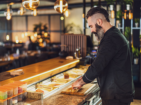 gewerbeversicherung mann mit bart bereitet sushirollen vor